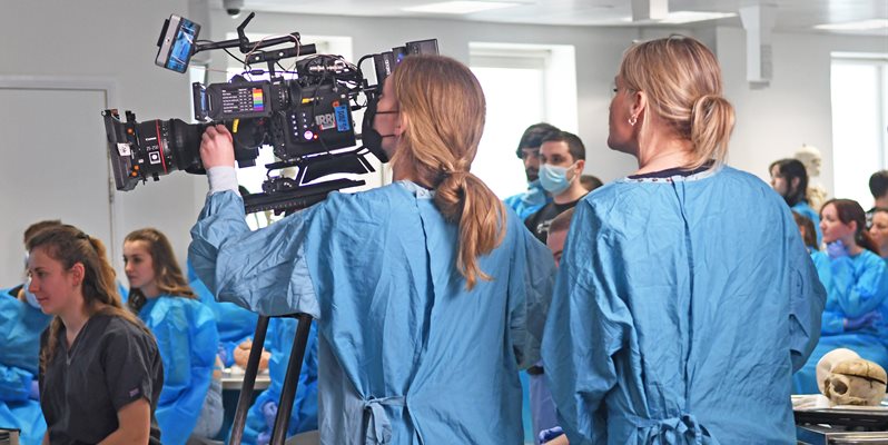 A film crew in blue scrubs filming in an anatomy lab