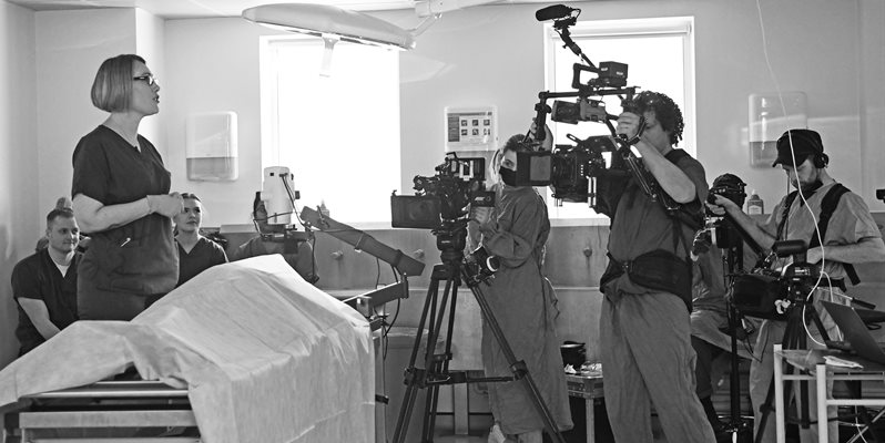 A black and white photo of a professor being filmed by a TV crew whilst talking to students