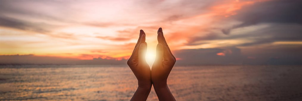 Summer sunset with silhouette of a young woman's hands on the beach holding the sun