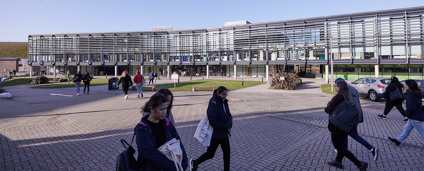 University students walking on Falmer campus with the Checkland Building behind