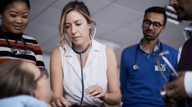 A female student practises using a stethoscope during a clinical teaching session