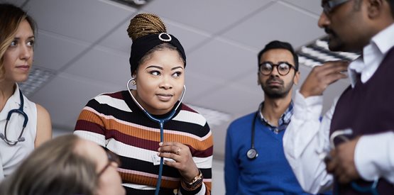 A student with a stethoscope listens to another's heart, others watching and teacher explaining