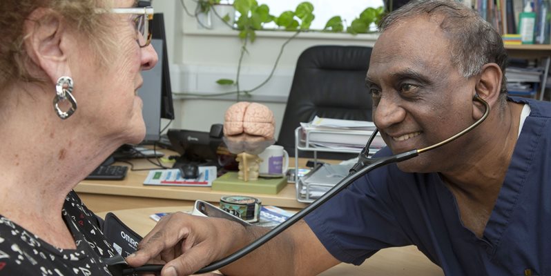 A patient being examined by a doctor in blue scrubs with a stethoscope