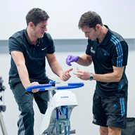 Two men talking, one on an exercise bike