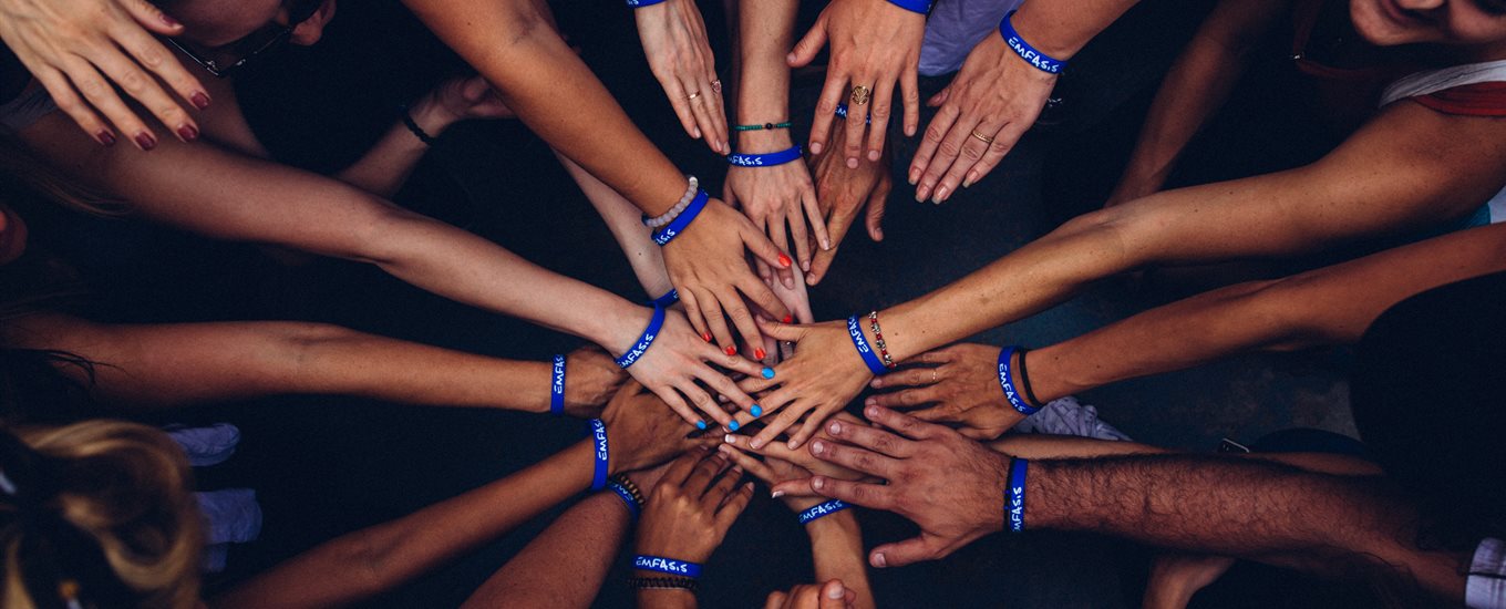 many different hands with different skin tones meeting together to touch. All are wearing blue bands. On hand has blue painted fingernails, another red.