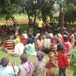 Group photo from an African village - people sitting on the floor listening to a speaker