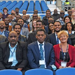 A group of people sat on blue seats at the AMEX football stadium looking into the camera