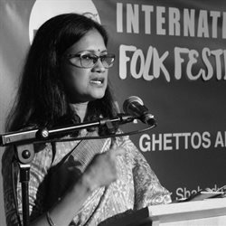 Dr Papreen Nahar presenting at an event in front of a microphone and sign. The photo is black and white. Photo credit Mr Ruhul Joy