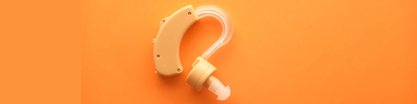 Flat lay image of a hearing aid on an orange background