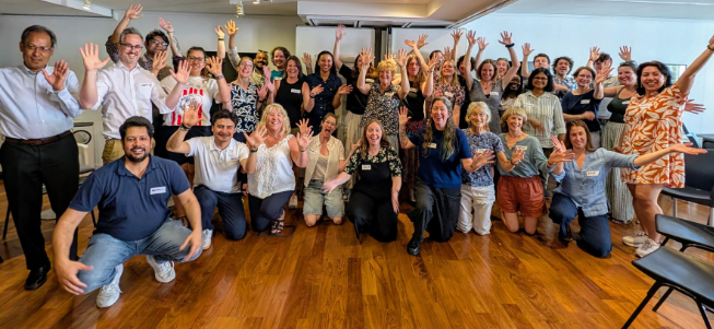 A group of people with arms in the air and smiling inside a building