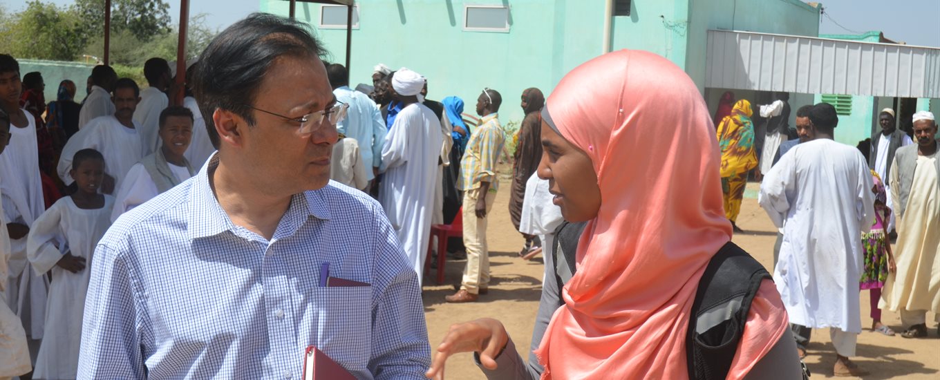 Researcher outside talking to a woman in a peach head scarf with others looking on