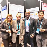 Four HIV researchers wearing lanyards and stood next to posters at a conference