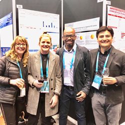 Four HIV researchers wearing lanyards and stood next to posters at a conference