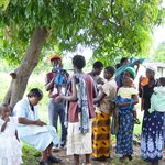 people pictured under a tree in Africa, including men women and children