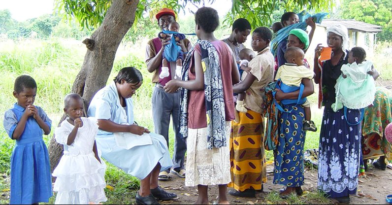 people pictured under a tree including men, women and babies in Africa