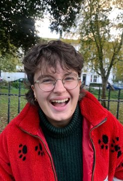 A photo of Daisy Boston outside in front of green trees in a red jacket