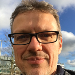 A head shot of Prof Florian Kern from BSMS, stood outside with a blue sky and clouds wearing glasses