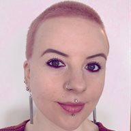 An image of a woman with pink hair and a striped top looking in to the camera