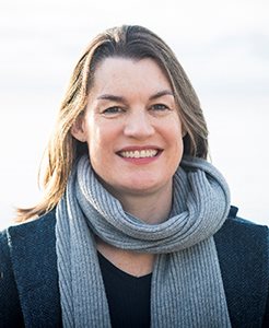 A women pictured wearing a scarf and jumper smiling at the camera