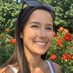 Lizzie Cross smiling with sunglasses in front of a flower patch