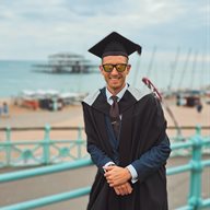 A man wearing a graduation outfit in front of the west pier in Brighton