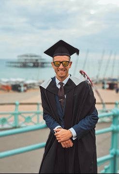 A man wearing a graduation outfit in front of the west pier in Brighton