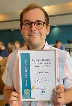A photo of Seb Shaw in a striped shirt holding a cerificate