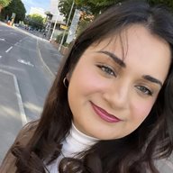 A photo of a girl with brown hair and white top, titled and looking to the right of the camera with pavement in the background