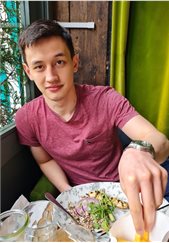 BSMS student Peter Preston leaning on a window eating food with a green curtain behind him