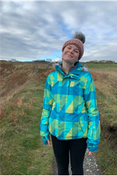 An image of a student, Robyn Creeden, wearing a hat and coat stood in a field on a cloudy day