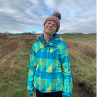 An image of a student, Robyn Creeden, wearing a hat and coat stood in a field on a cloudy day