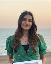 A girl standing on the beach with the sea in the background with a sunset in the sky, wearing a green top