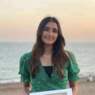 A girl standing on the beach with the sea in the background with a sunset in the sky, wearing a green top