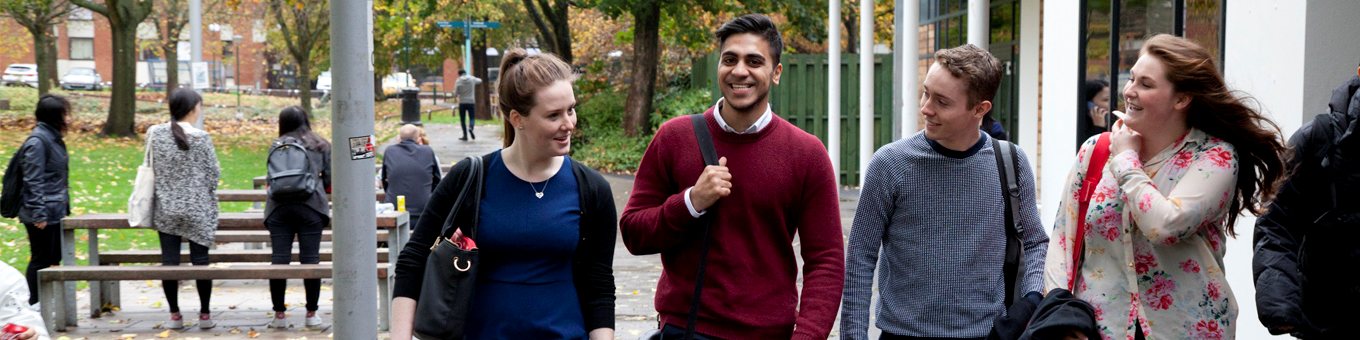 Four students walk through campus smiling